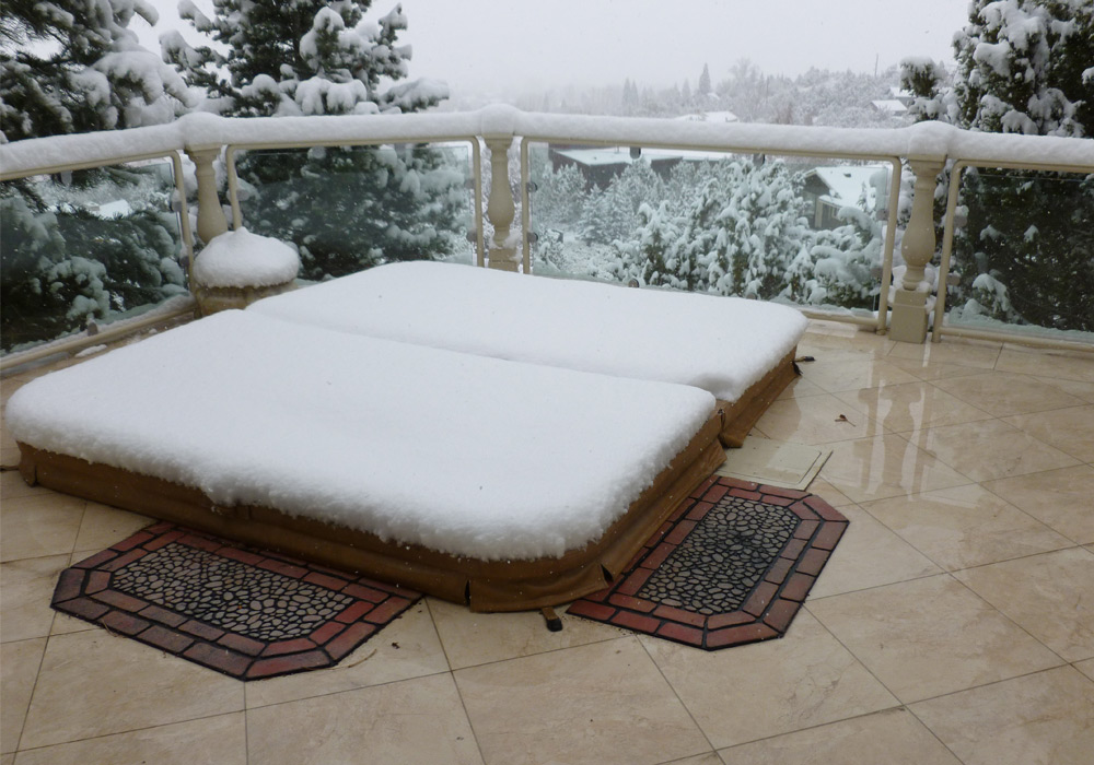 A snowy view in Tahoe of a hot tub deck with radiant heat pavers; the heated pavers do not have snow on them, but the hot tub cover and deck rails do.